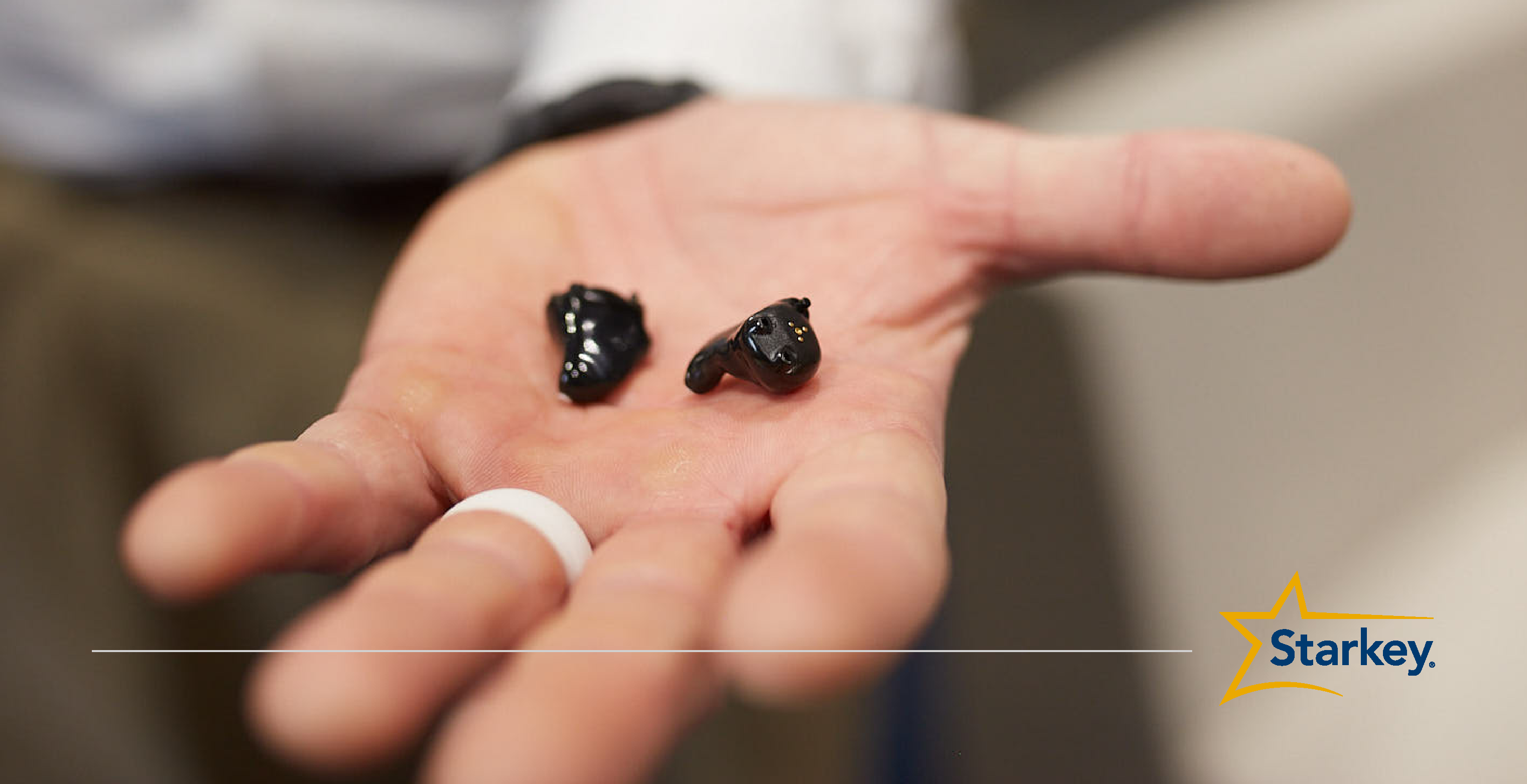 Black In-the-canal custom rechargeable hearing aids in the palm of man's left hand